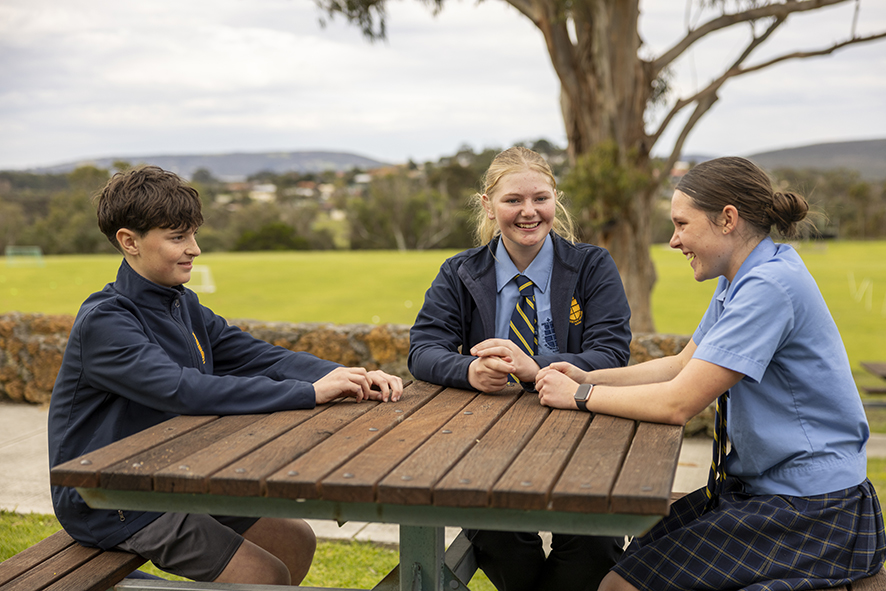 Students from St Joseph's College sitting at a picnic table, smiling.