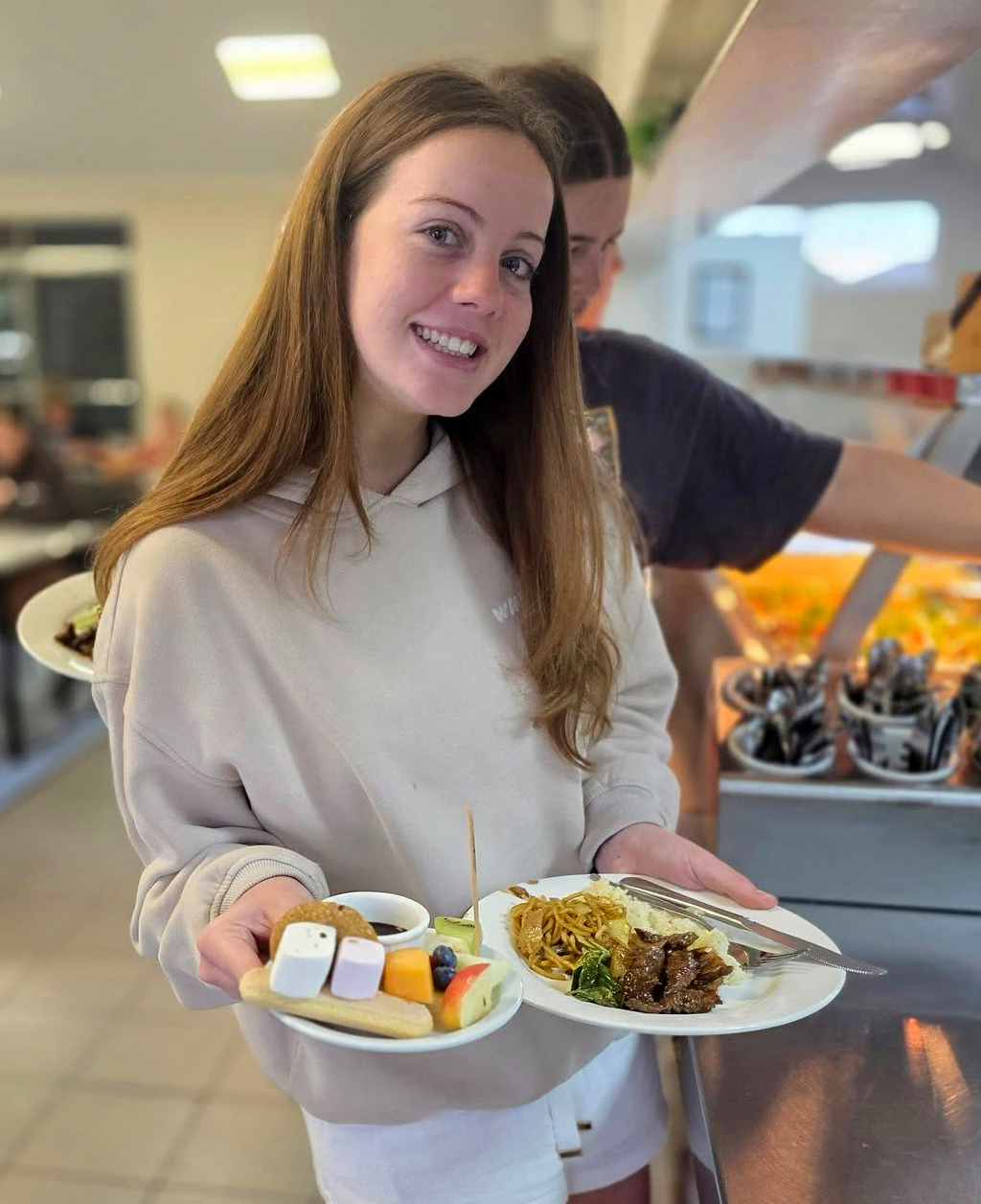 A boarder from Geraldton Residential College smiling and showing her delicious dinner and dessert plates.