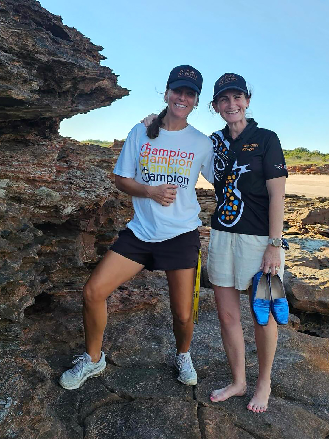 2 boarding supervisors from Broome Residential College, smiling, standing on rocks by the beach.