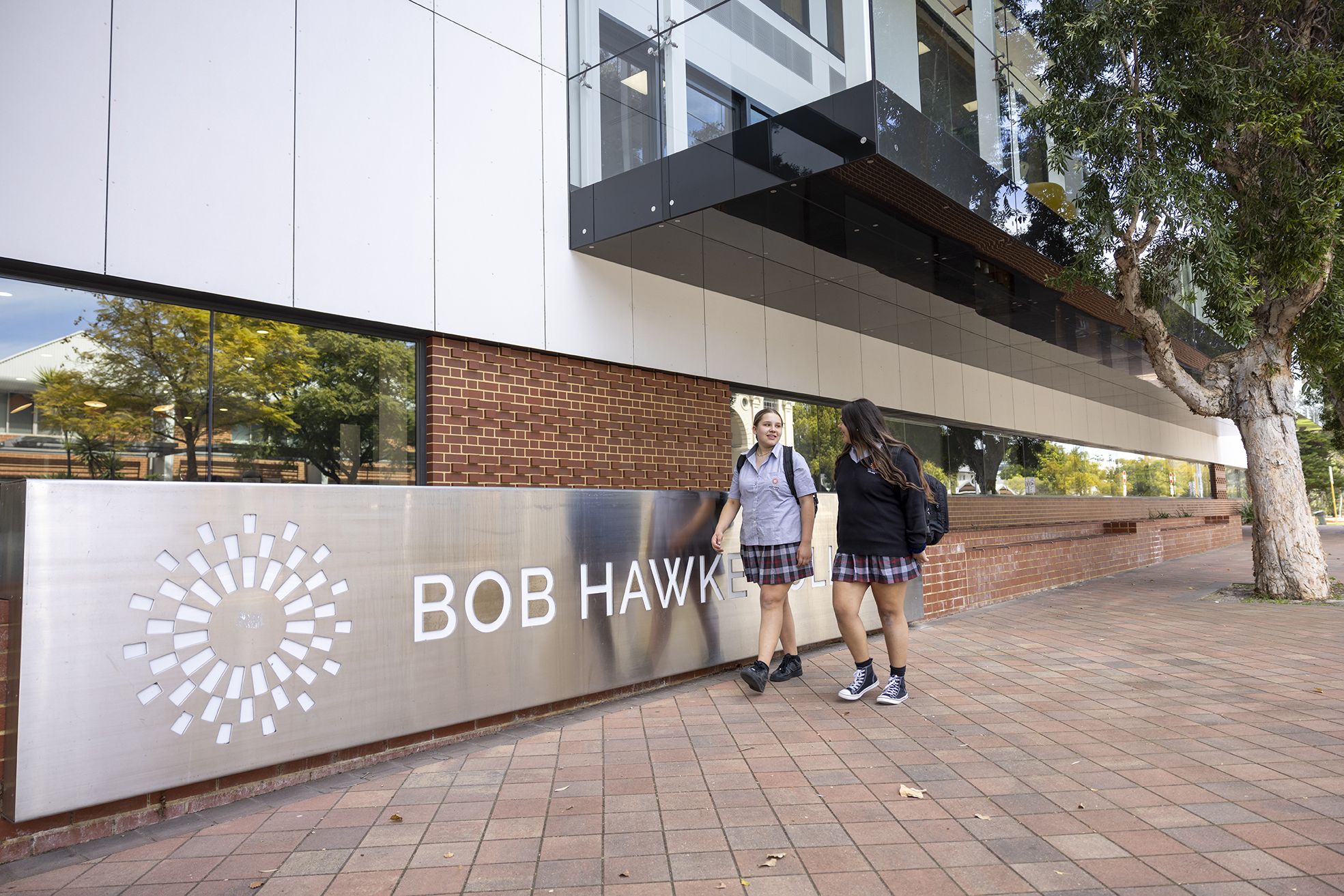 2 students walking in front of the Bob Hawke College sign.