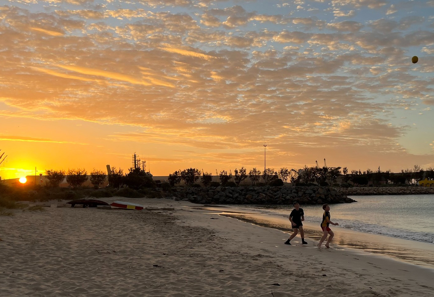 Boarders from Geraldton Residential College playing footy on the beach at sunset.