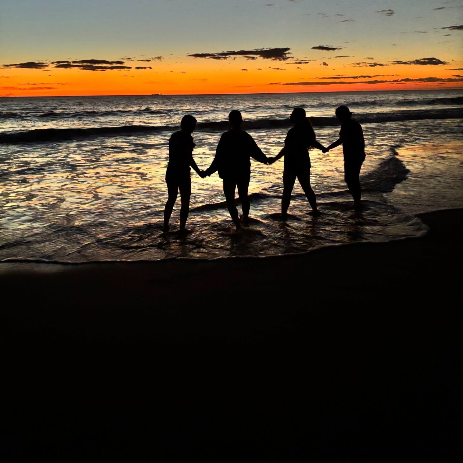 City Beach Residential College boarders holding hands at the edge of shore with a sunset background.