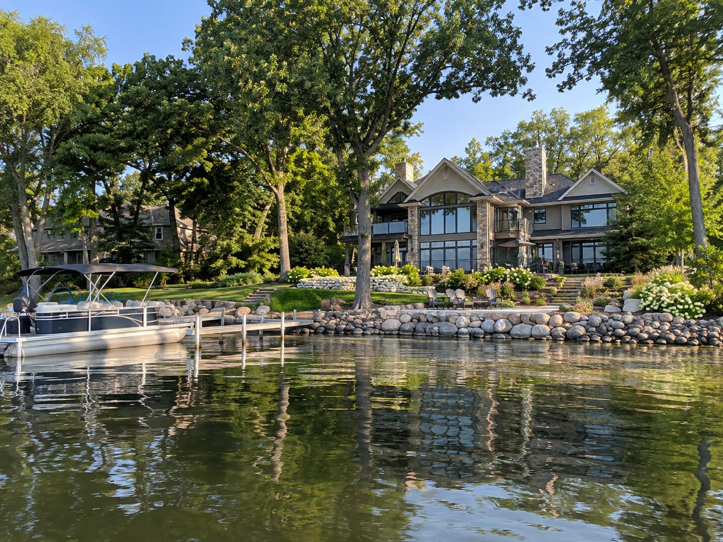 Lakeside home with mature trees, a dock, and a pontoon boat