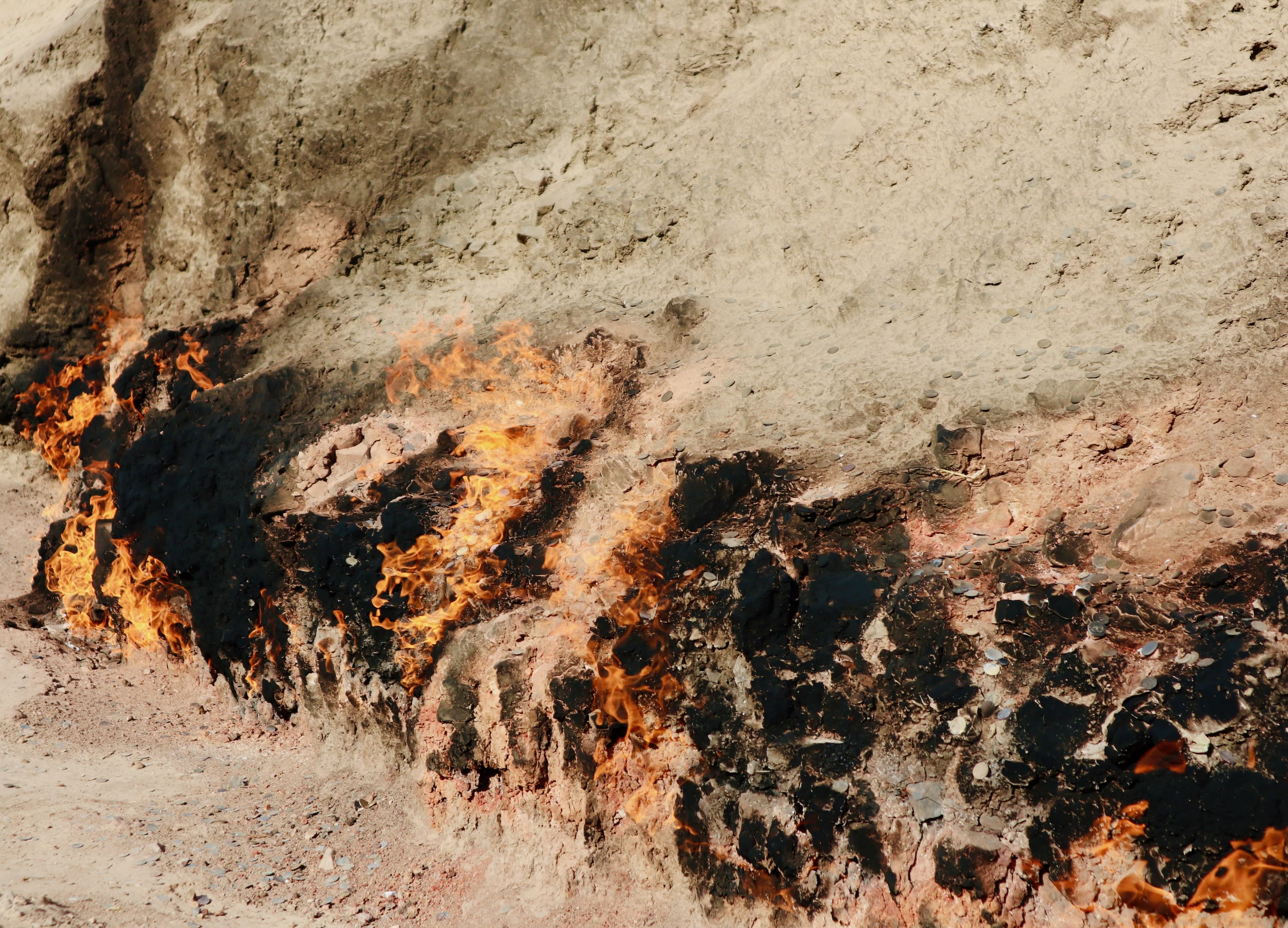 A natural gas fire known as Yanar Dag burns on a hillside, with flames emerging from the ground. The surrounding terrain, reminiscent of Gobustan's sandy and rocky landscapes, highlights the unusual and striking phenomenon of perpetual fire.