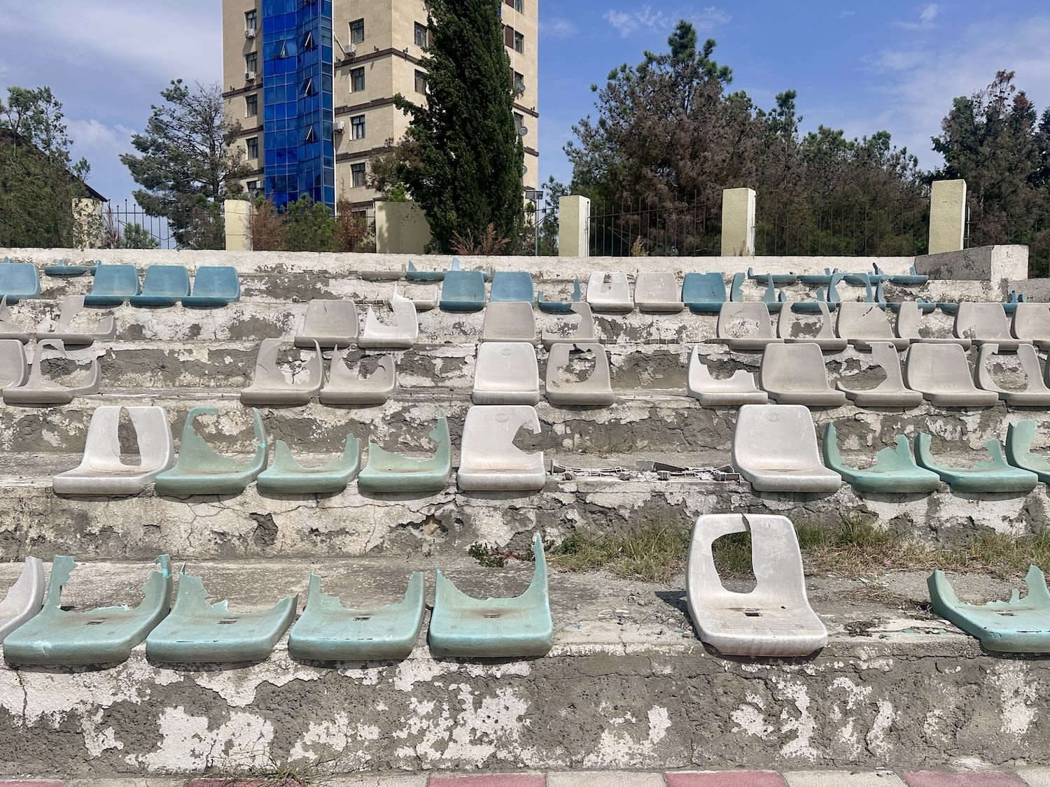 Dilapidated stadium seating with missing and damaged blue and white chairs.