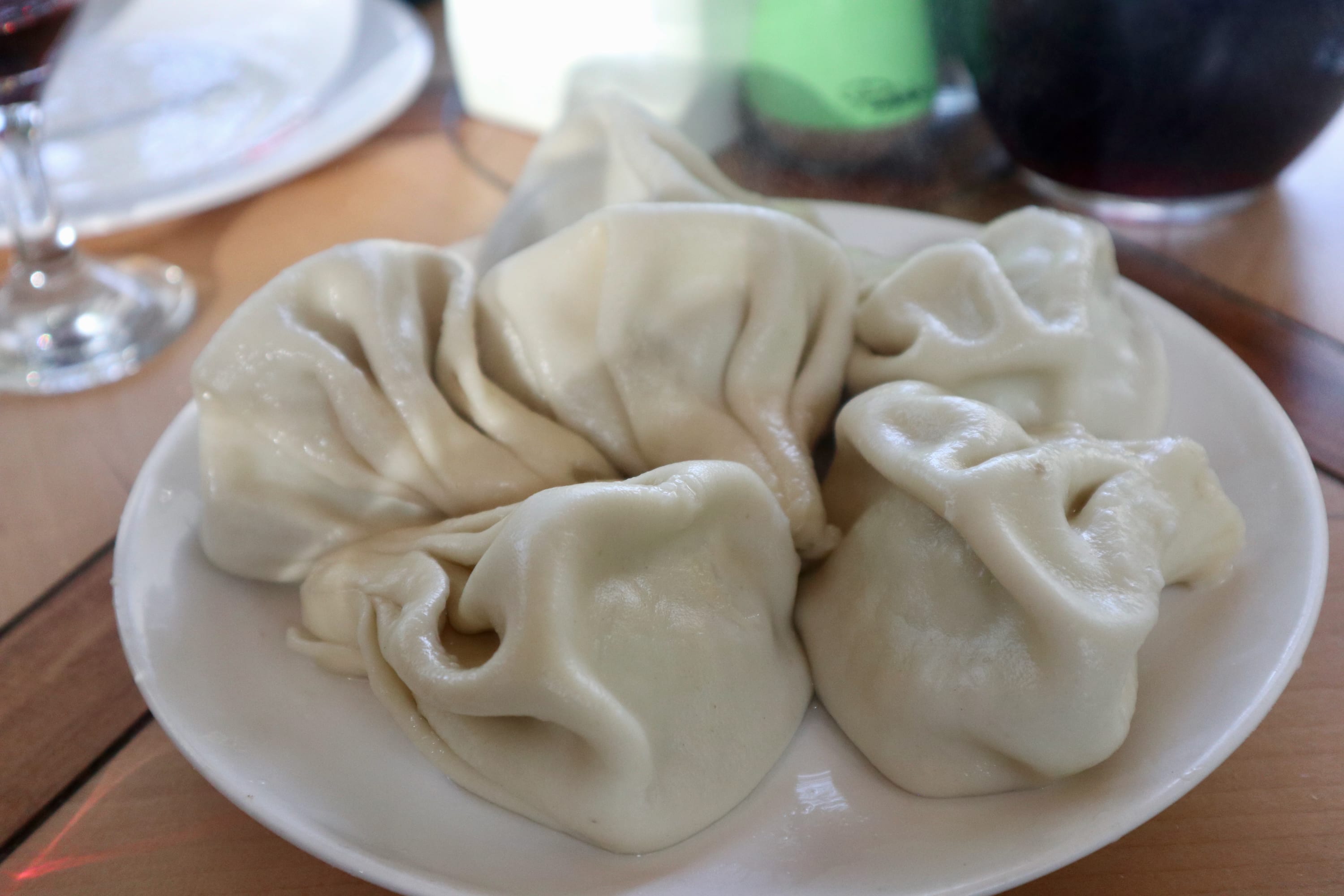 A plate of steamed dumplings on a wooden table, with a glass to the side in the background, captures one of the must-see spots for any food lover during Georgia travel. This culinary experience is just one reason why many wonder, is Georgia worth visiting? The local highlights certainly make it an enticing destination.