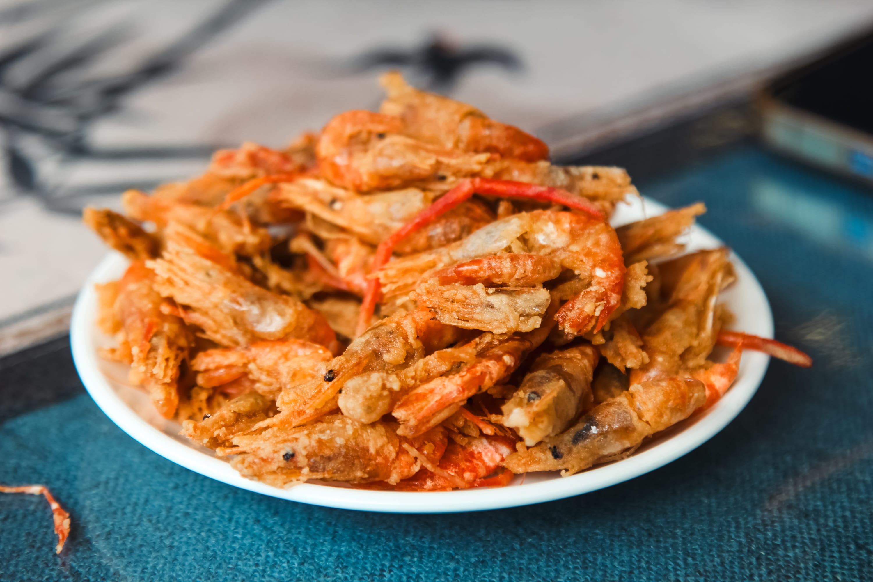 A white plate filled with crispy fried shrimp sits on a blue surface, reminiscent of dishes enjoyed on a Guilin to Yangshuo cruise, showcasing the golden-brown color and crunchy texture of the shrimp.