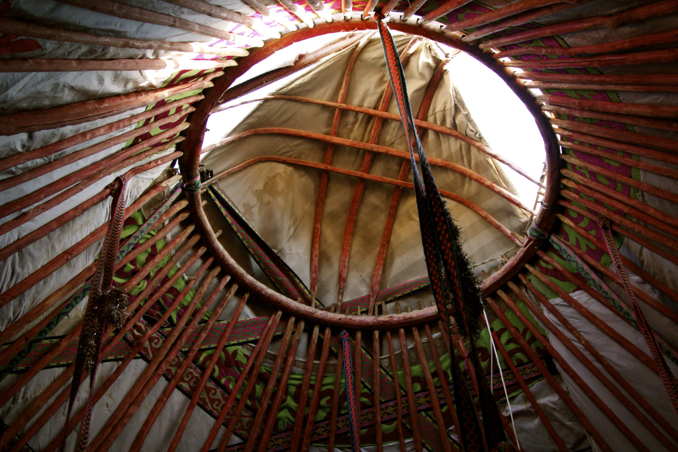 Interior view of a yurt, reflecting Uyghur culture, with the circular roof opening framed by wooden supports and colorful fabric decorations. Natural light streams in from above, highlighting the intricate patterns and craftsmanship reminiscent of Xinjiang's stunning landscapes.