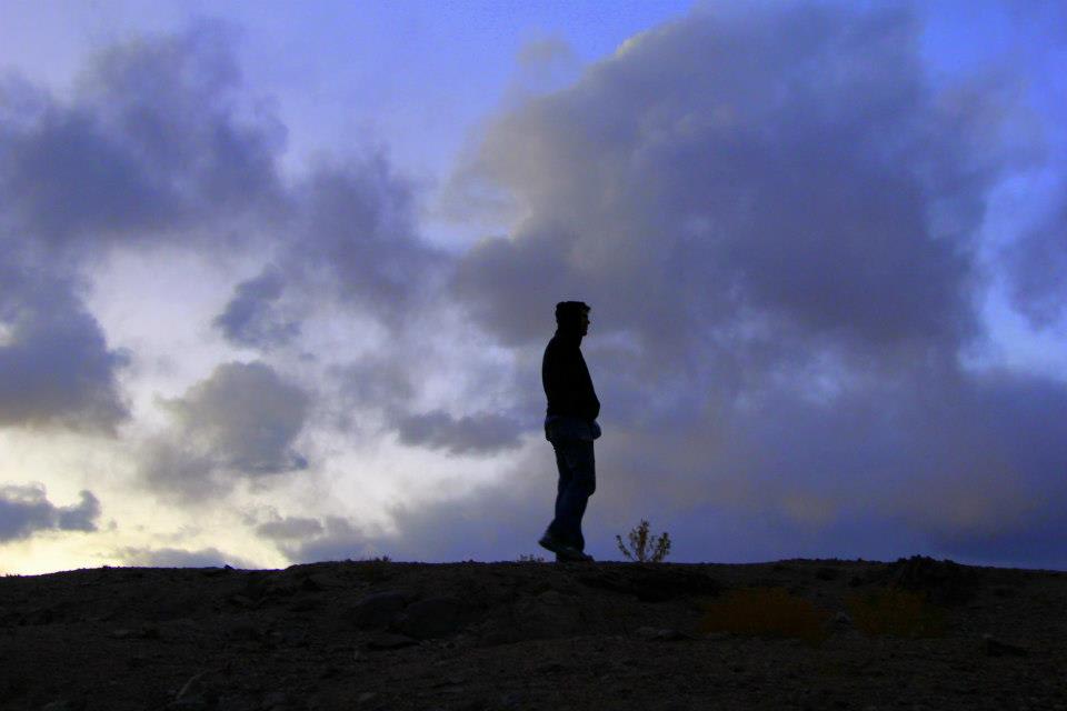 Silhouette of a person standing on a hill at dusk, set against the dramatic sky filled with clouds, reminiscent of Xinjiang's stunning landscapes.