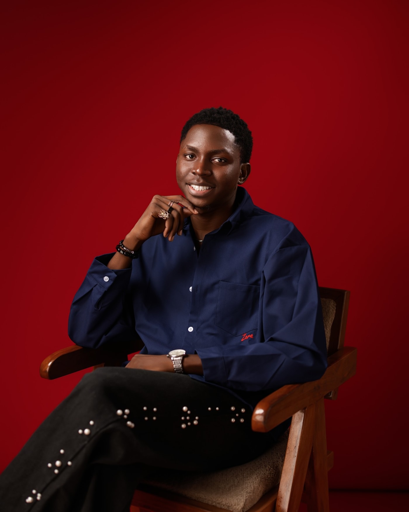 Oluwafemi Oduneye smiling, seated in a navy shirt against a red backdrop