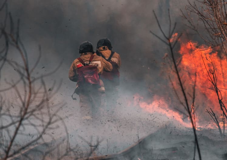 Two firefighters walking amidst smoke and flames outdoors
