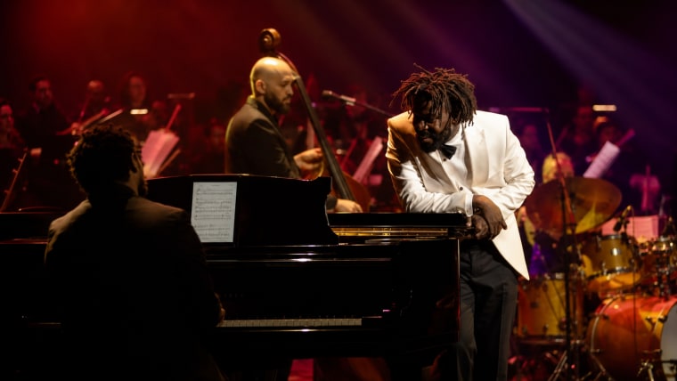 Editorial visual representing Mandisi Dyantyis’ Symphonic Celebration at Teatro Montecasino, featuring a full orchestra, trumpet-stage lighting, theatre-scale grandeur, jazz and gospel textures, deep purple shadows, gold highlights and premium Viranova glass styling.