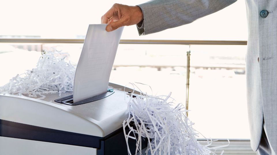a photograph of a person in a suit in an office who is shredding a document in a commercial shredder.