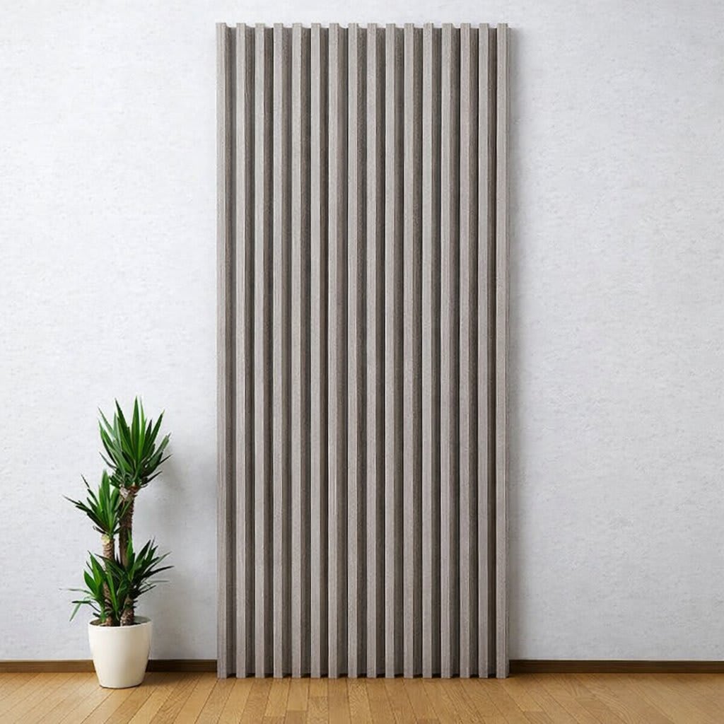 A tall, vertical WPC wall panel with light gray textured slats stands out against a light-colored wall in a minimalist, modern interior, paired with a small potted plant on a warm wooden floor, creating a serene and clean design.