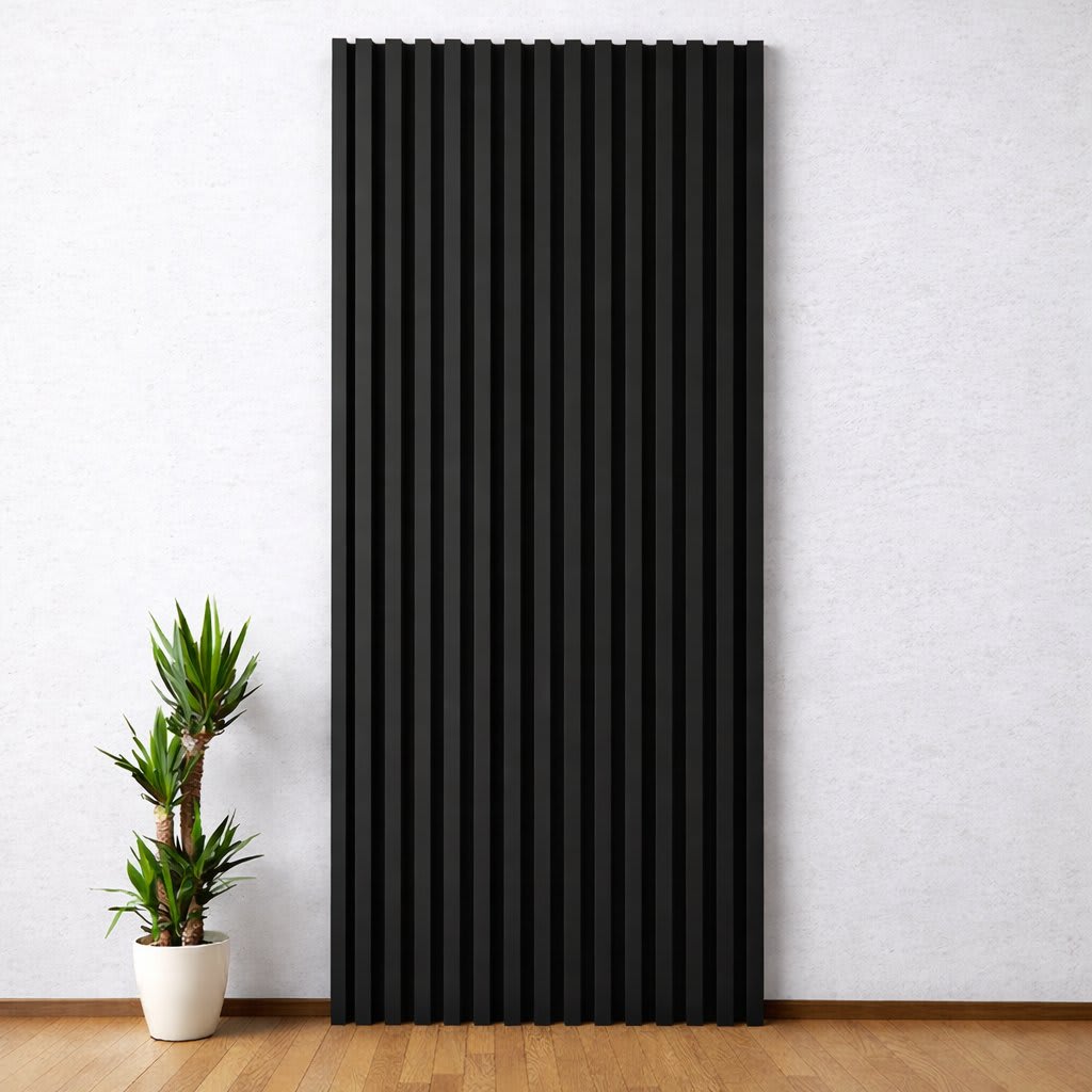 A tall, vertical WPC wall panel with matte black textured slats stands out against a light-colored wall in a minimalist, modern interior, paired with a small potted plant on a warm wooden floor, creating a serene and clean design.