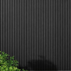 WPC slatted wall panels in black tones, featuring uniform vertical slats and a natural wood grain texture, framed by green foliage and soft shadows. A minimalist architectural facade ideal for backgrounds, exteriors, design, and nature-inspired concepts.