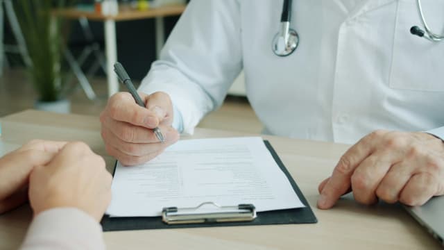 A doctor filling in notes on a clipboard during a patient consultation