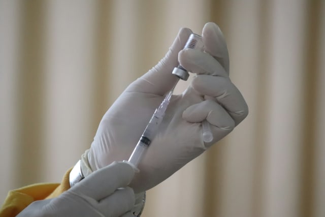 A gloved hand drawing a vaccine dose from a vial into a syringe