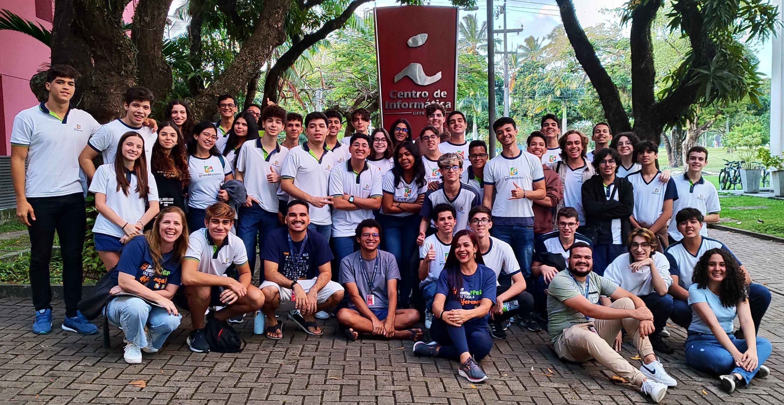 Estudantes e integrantes do PET Informática em frente do Centro de Informática sorrindo e fazendo poses divertidas após uma visita.