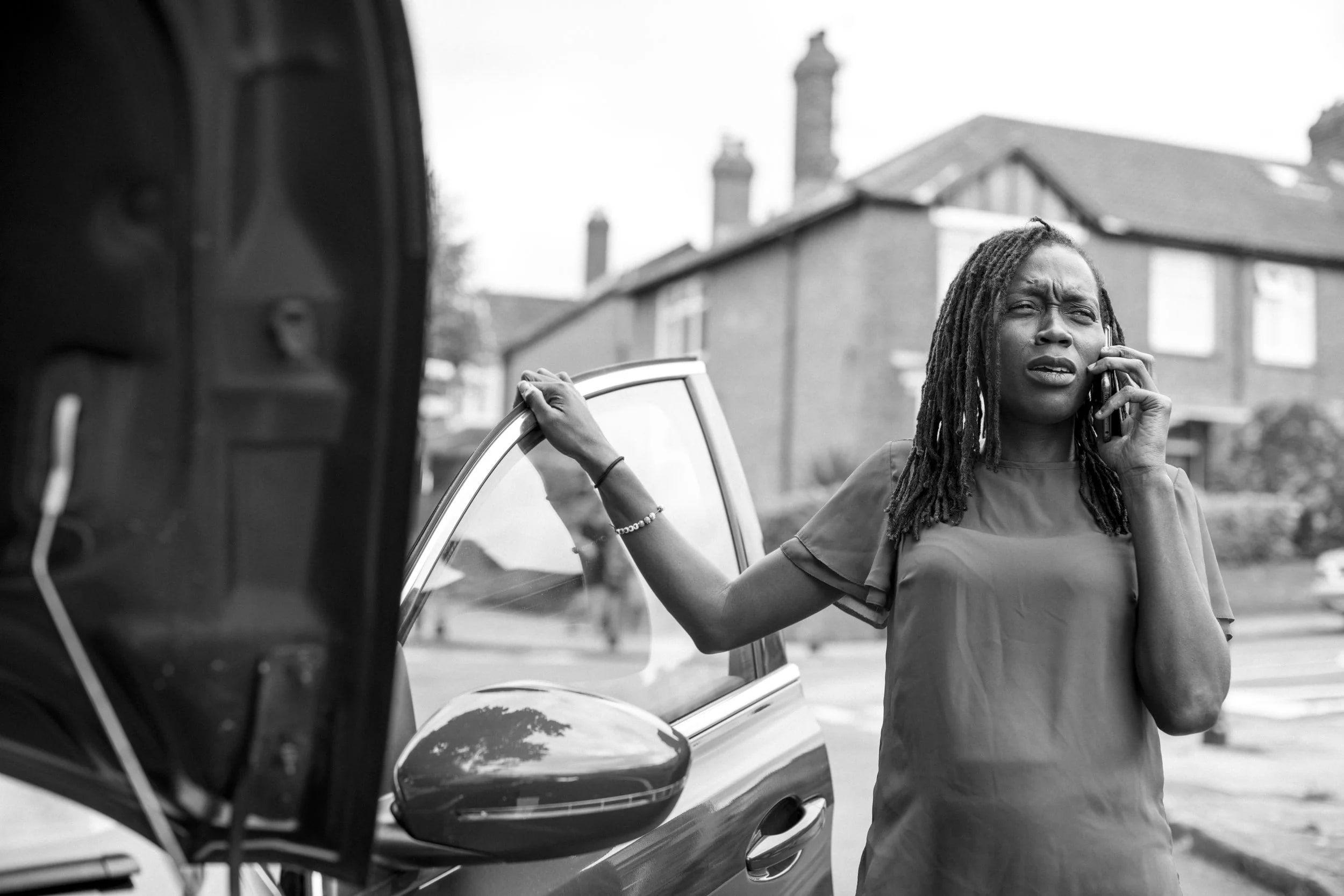 Black and white photo of woman talking on phone next to a car after incident