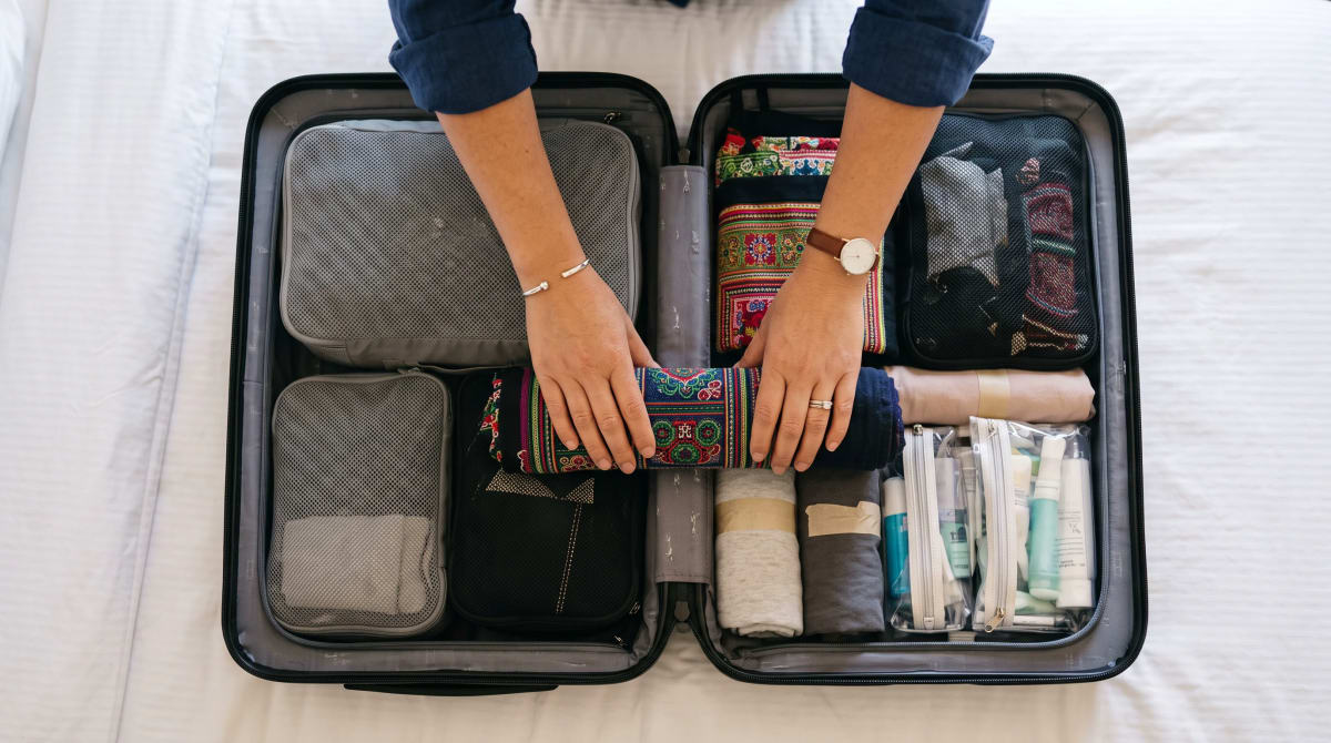 Overhead view of hands packing clothes into a suitcase on a hotel bed