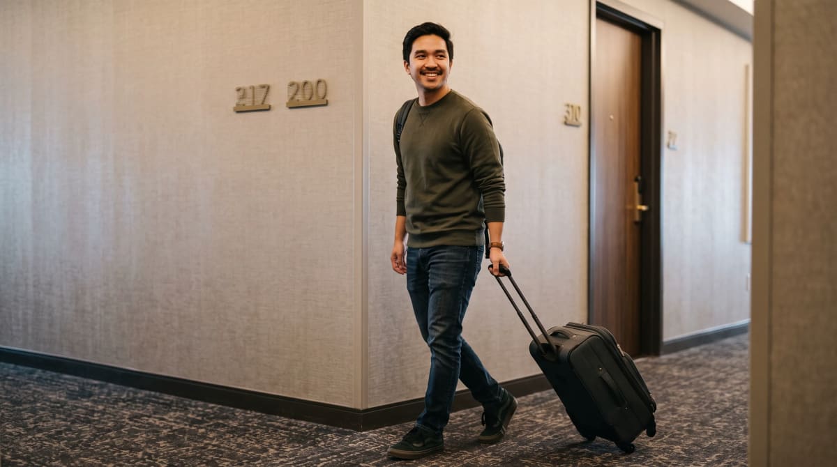 Traveler pulling a suitcase around a quiet hotel corridor corner