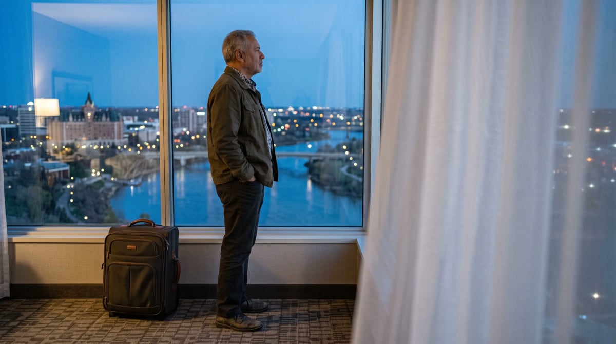 Traveler in profile at a hotel-room window facing a city skyline