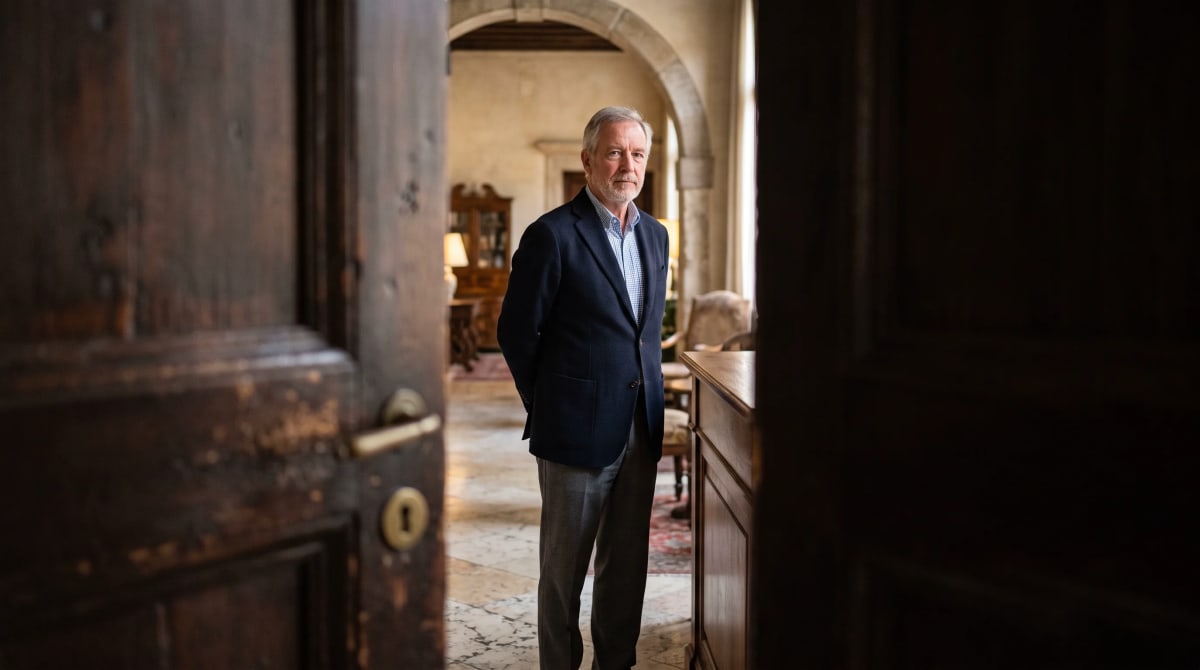 Traveler in a navy blazer at a hotel concierge desk, seen through a staff doorway in mid-morning
