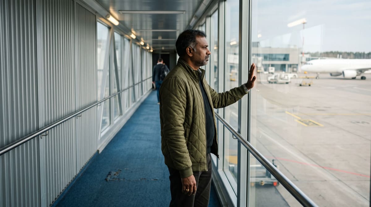 Traveler at a jet bridge window in Kaunas, palm on the glass, in profile
