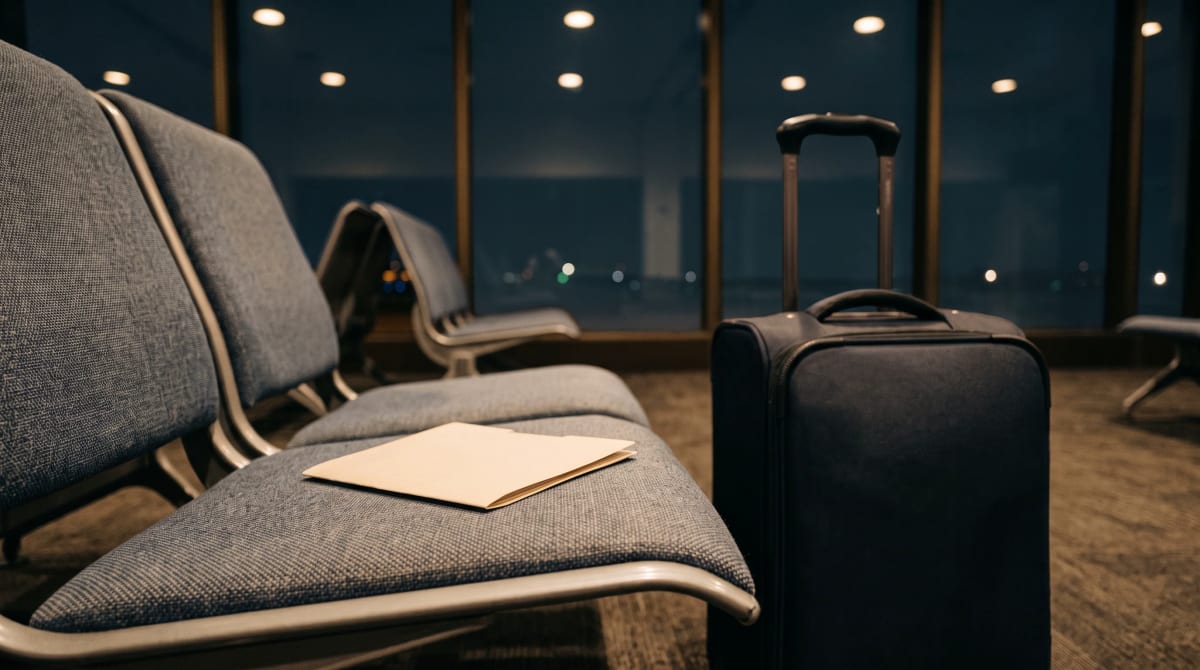 Plain key folder on an empty airport gate seat beside a closed suitcase under warm night downlights