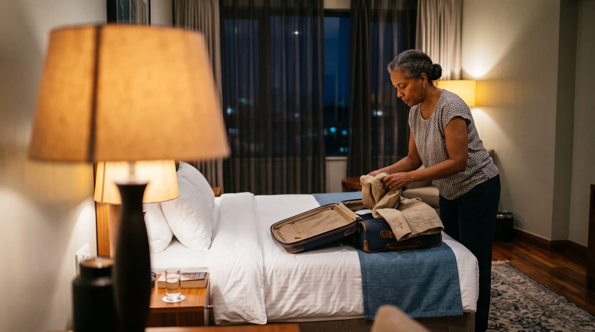Traveler folding a jacket into an open suitcase beside a lamp in a Nairobi hotel room