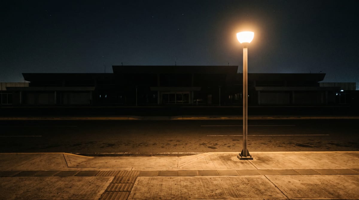 Empty airport curb at night with a single street lamp glowing beside a bare lane