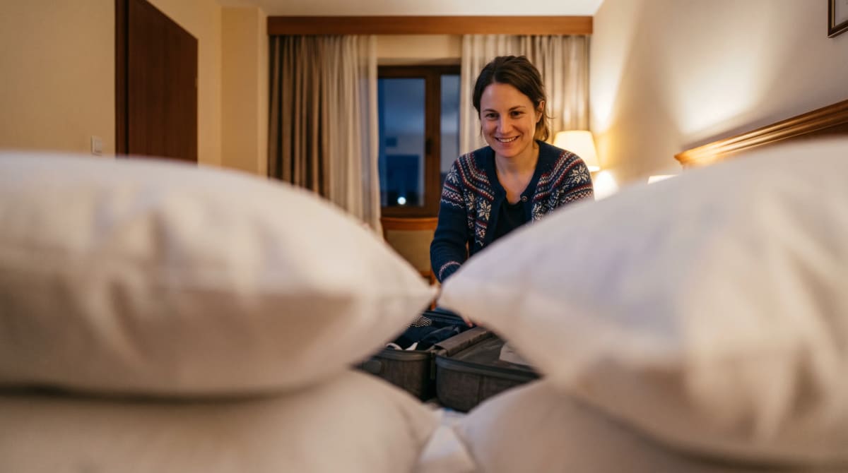 Traveler folding a sweater into an open suitcase on a hotel bed