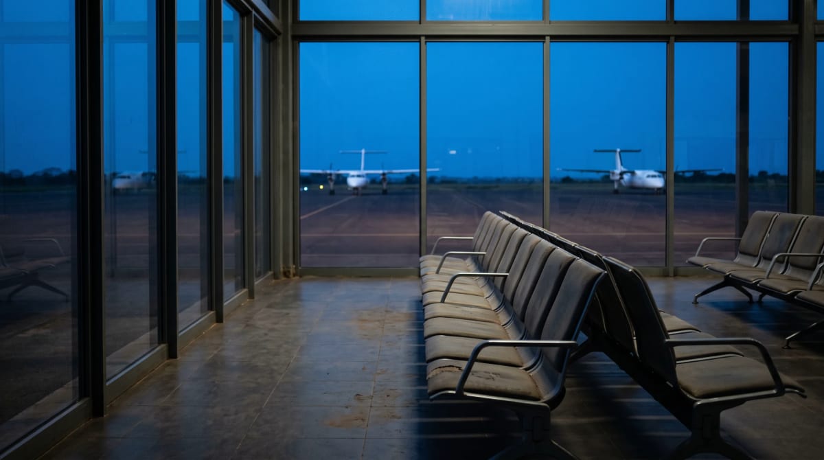 Two aircraft on a distant taxiway at dusk seen from a terminal window, with no airline markings or readable signs