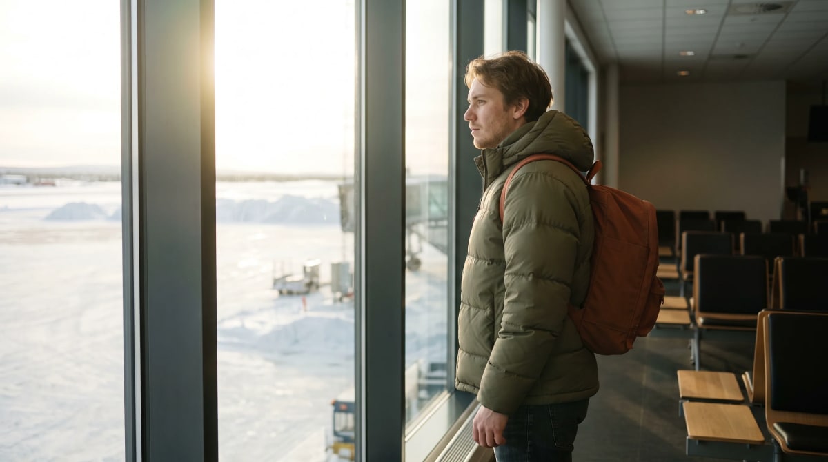 Traveler with a backpack standing at a tall airport gate window at midday