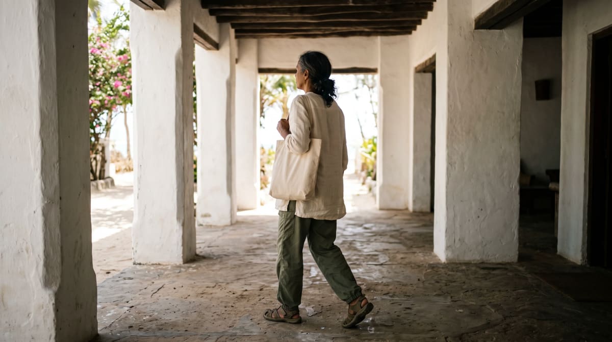 Traveler arriving with a canvas tote under a hotel porte-cochère in the afternoon