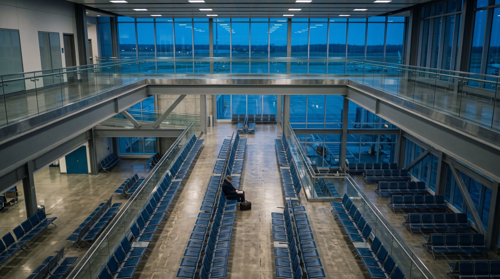 Traveler seated among empty airport gate seats with a paperback in the lap