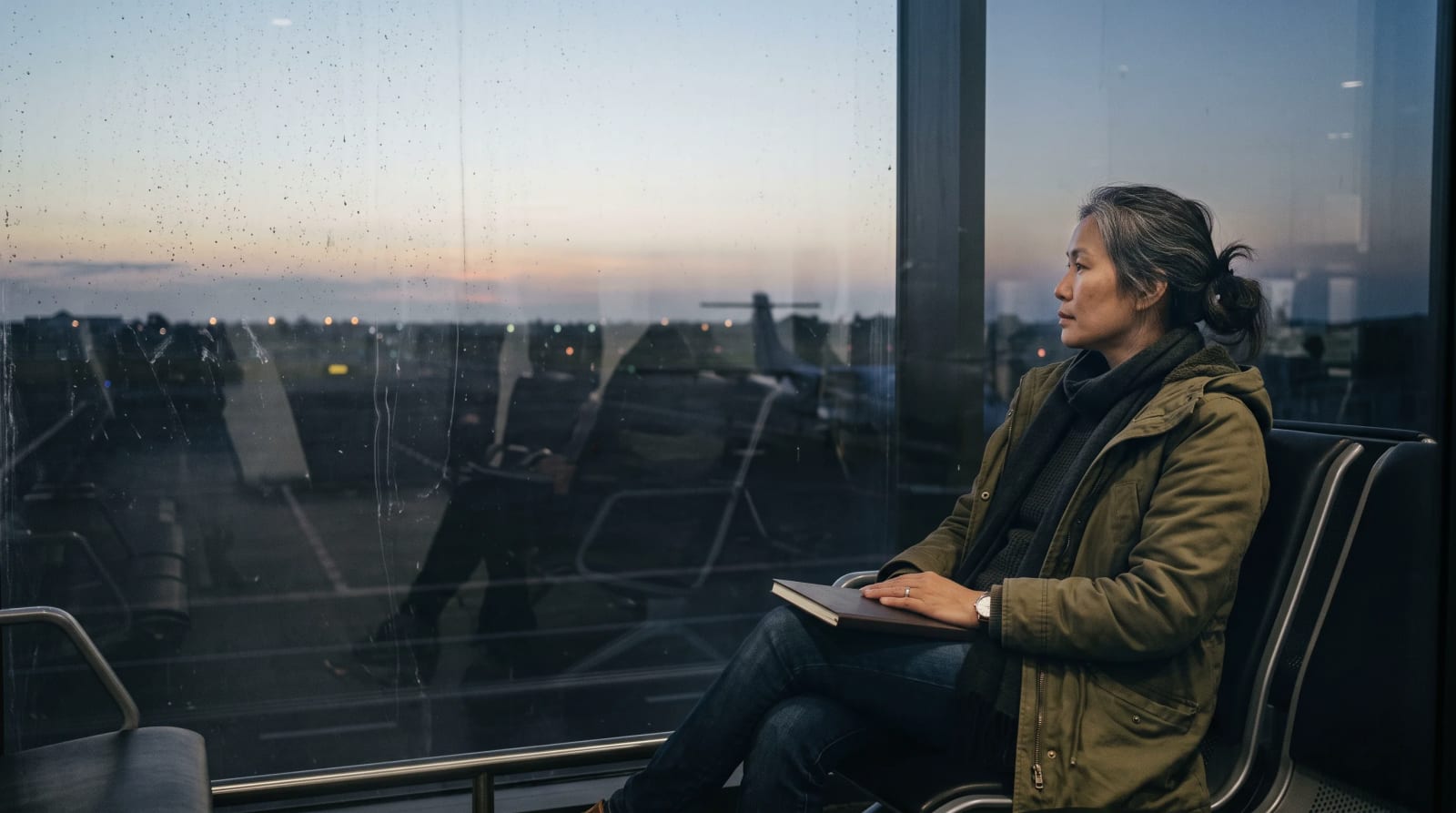 Traveler seated beside an airport window at dawn with a closed notebook on the lap