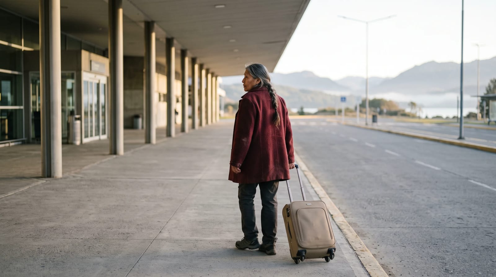 Traveler rolling a carry-on along a quiet airport departures curb in early morning light