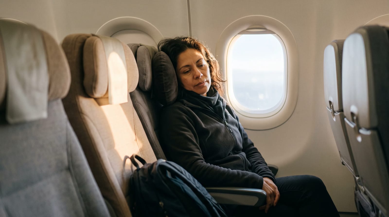 A traveler resting with a travel pillow in an aircraft cabin near a window toward Chicago