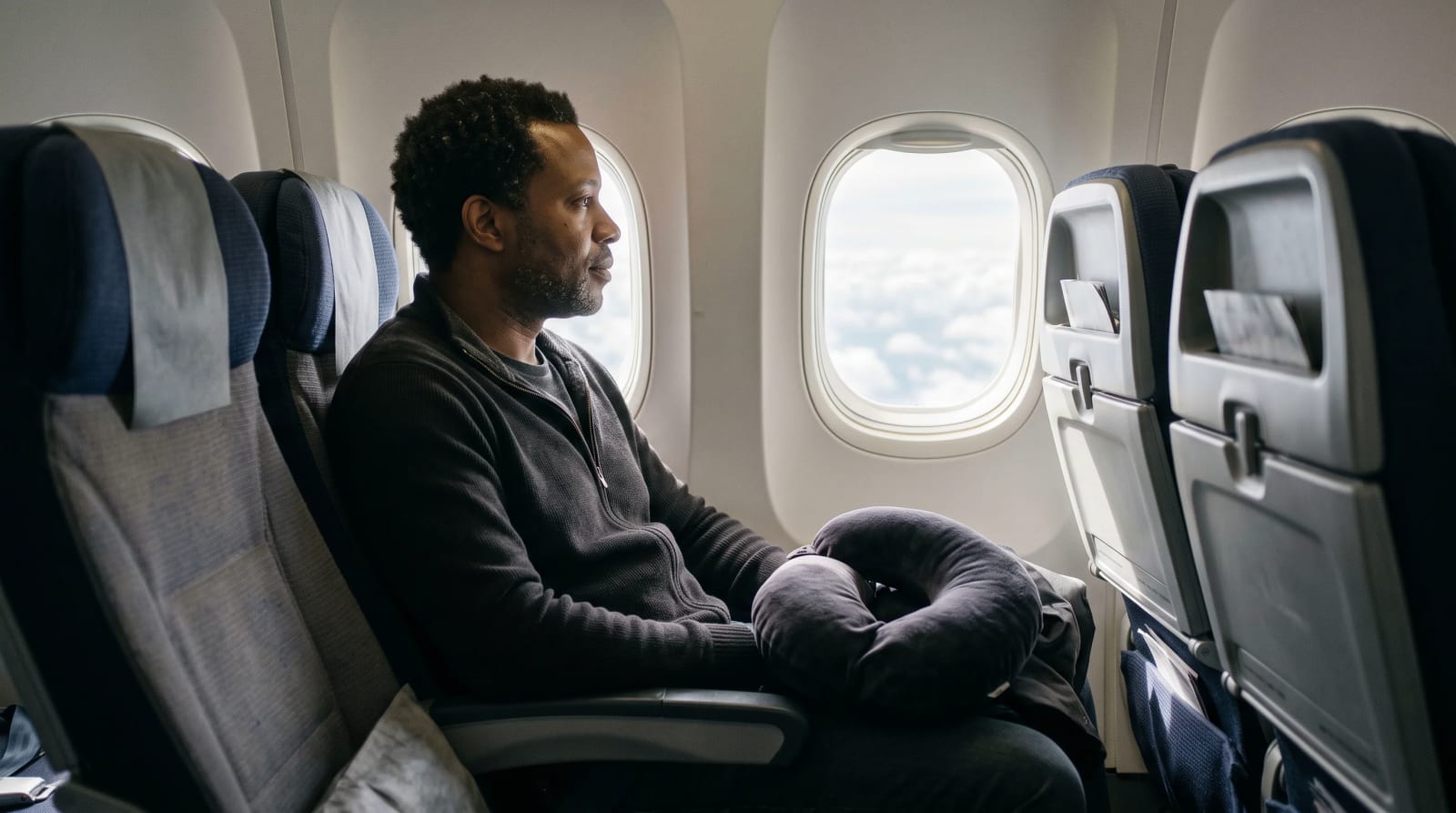 A traveler seated by an aircraft window with a travel pillow over Atlanta