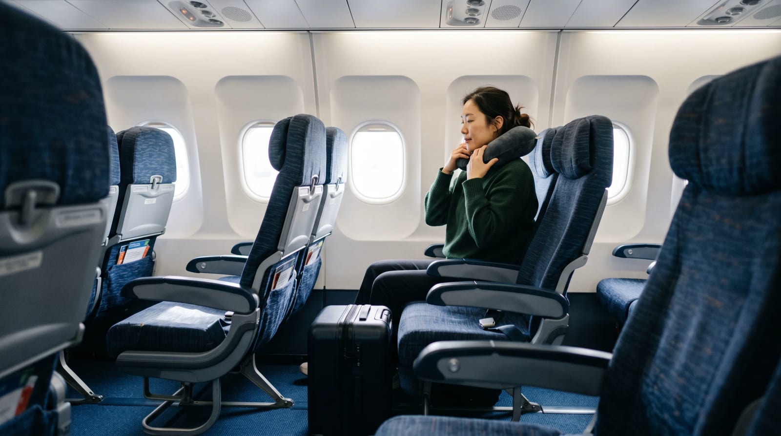 A traveler seated in a long-haul cabin with a travel pillow near New York