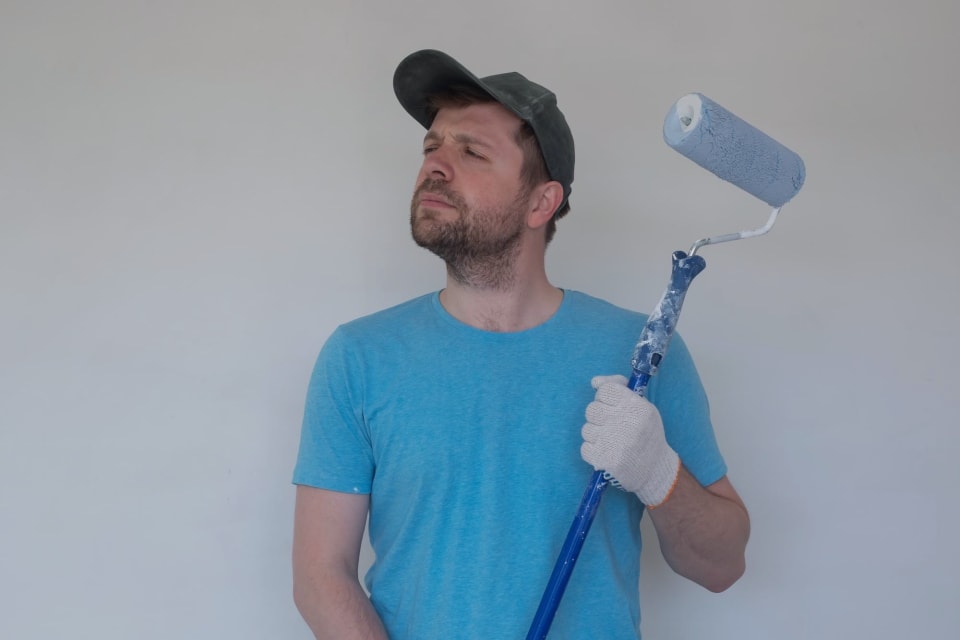 Pintor con gorra y guantes pasando el rodillo por una pared