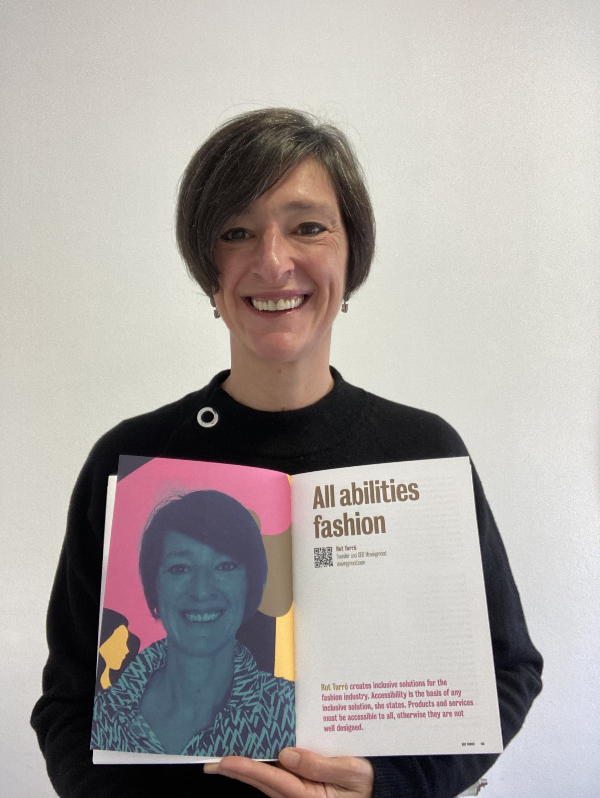 Rut smiling and holding the book open showing All Abilities fashion essay, inclusive fashion.