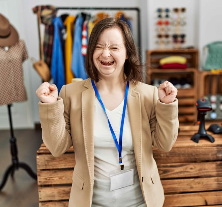 Mujer joven con síndrome de down trabajando como gerente en una boutique minorista emocionada por el éxito con los brazos levantados y los ojos cerrados celebrando la victoria sonriendo.