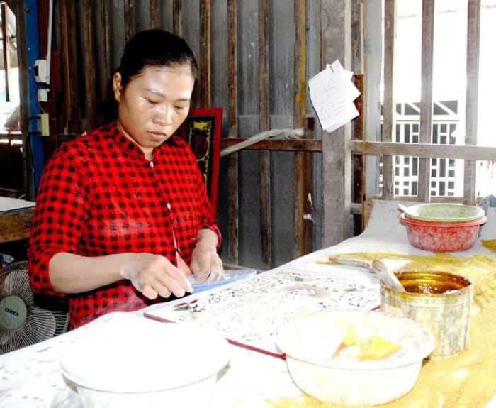 Người thợ ngồi vẽ chi tiết lên tấm kính đỏ