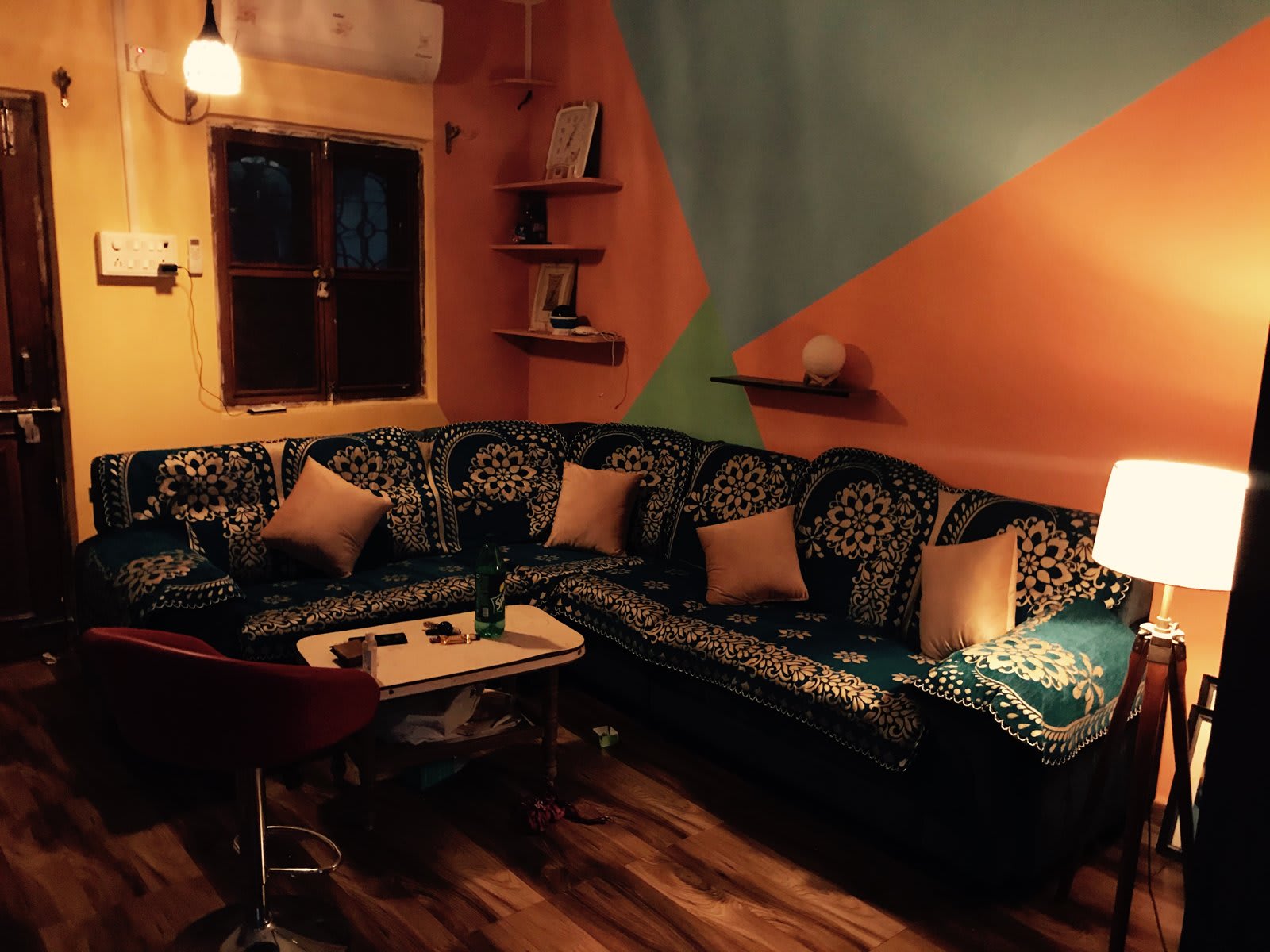 Finished living room with orange and teal geometric walls, patterned corner sofa and floor lamp