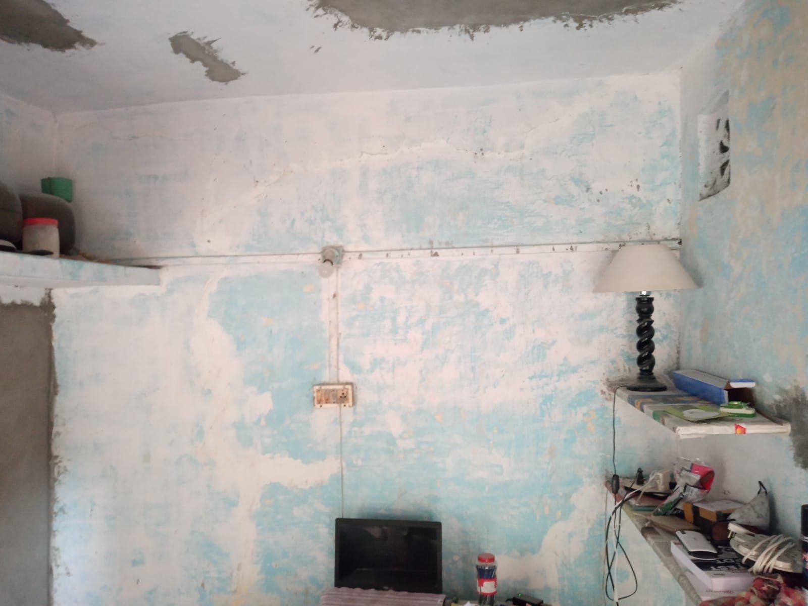 Wall with blotchy, flaking blue paint and exposed plaster patches