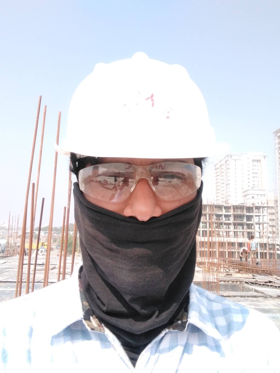 Sagar in a white hard hat, safety glasses and a dust mask on a slab with rebar starters behind