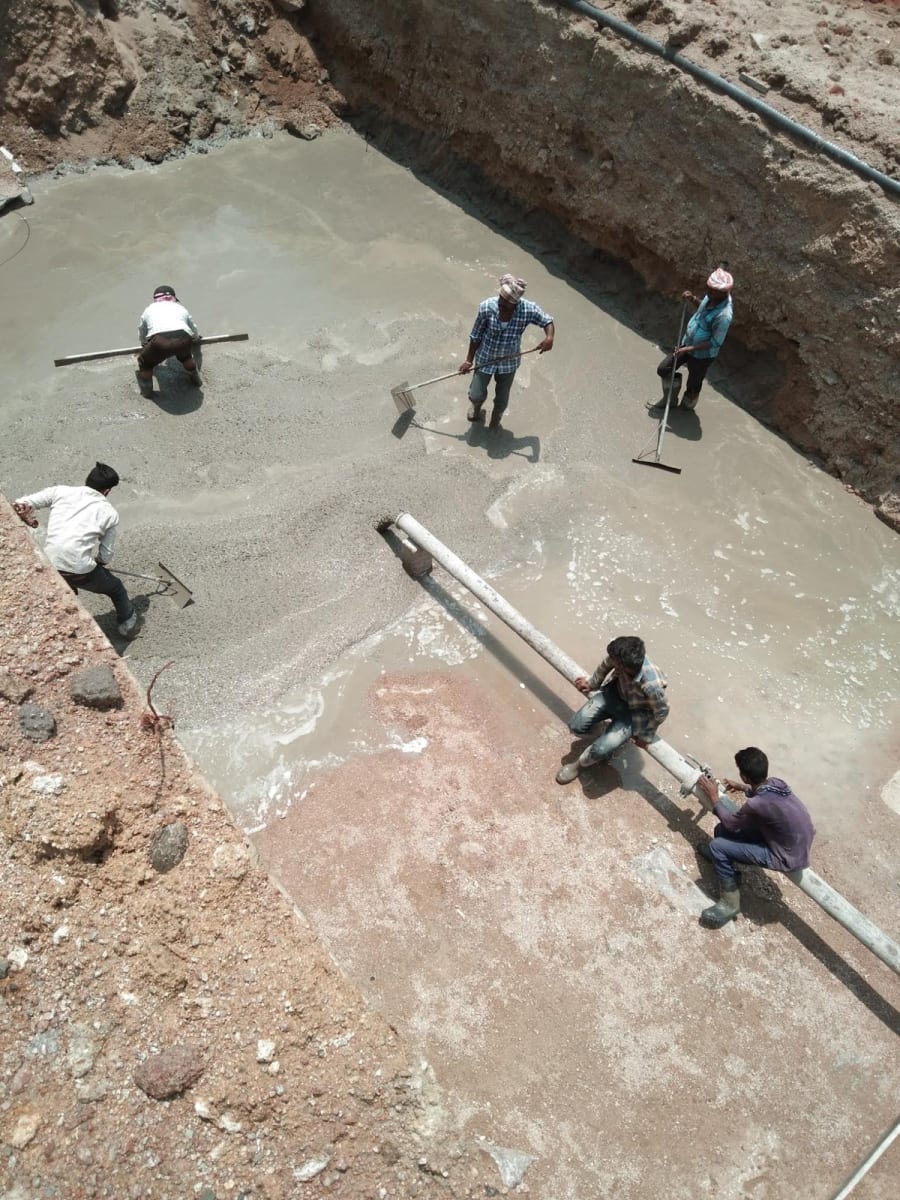 Workers spreading and levelling concrete in an excavation as it comes out of a pump pipe